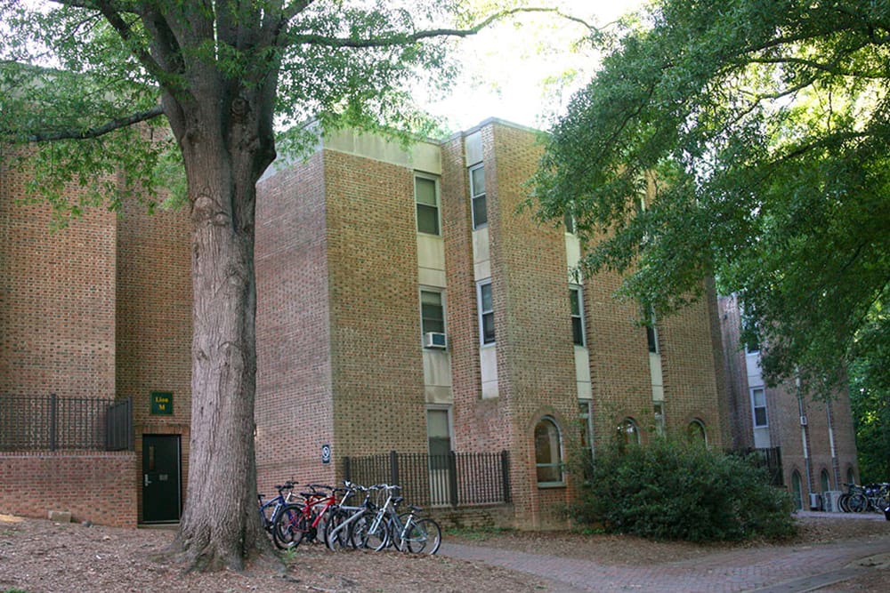 A three story brick building nestled amongst mature trees with a bike rack