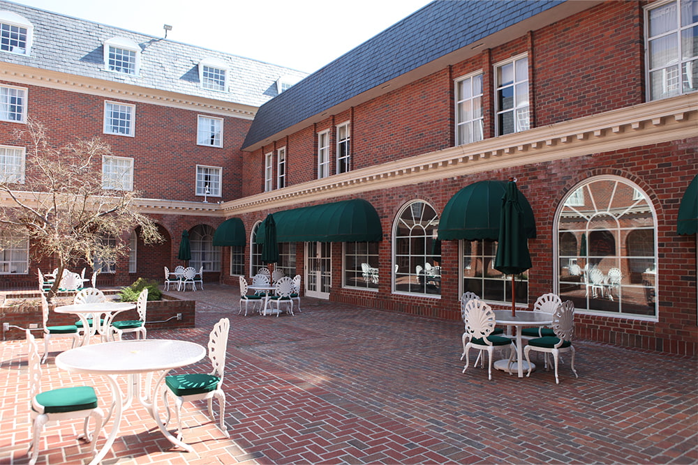 Brick, windowed dorm building with a patio that features numerous tables, umbrellas and chairs.