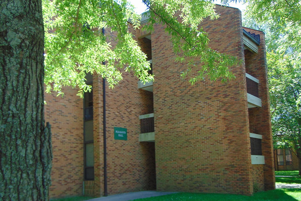 A three story brick building with exposed breezeways nestled in a wooded setting