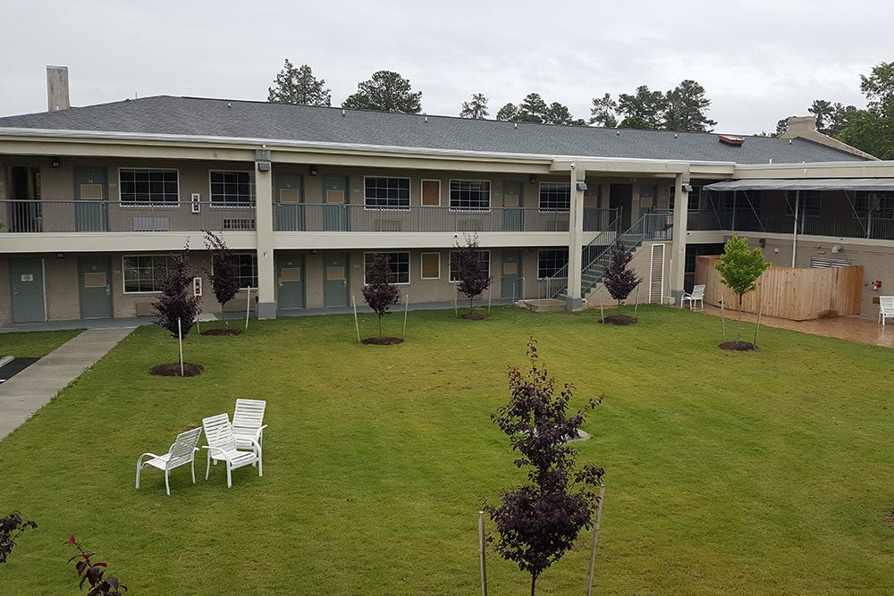 Two-story, outdoor dorm suite entrances with walkways next to a green lawn.