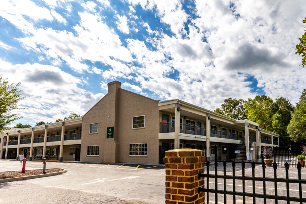 Front area of a brick dorm building next to a parking lot and iron fence. 