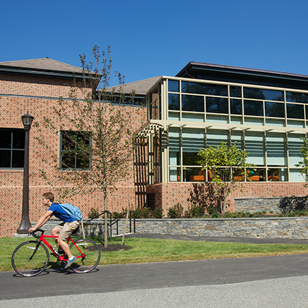 A student on a bicycle rides by a brick building.