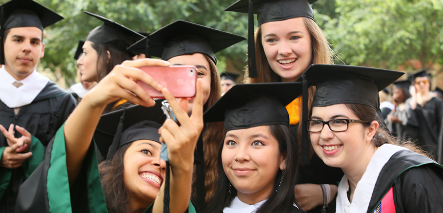 Group of graduates in caps and gowns taking a selfie outdoors.