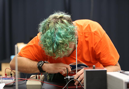 Person leaning over an electronics setup, working with wires and components.