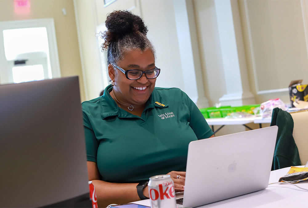 A person in a William & Mary polo smiles while using a laptop.