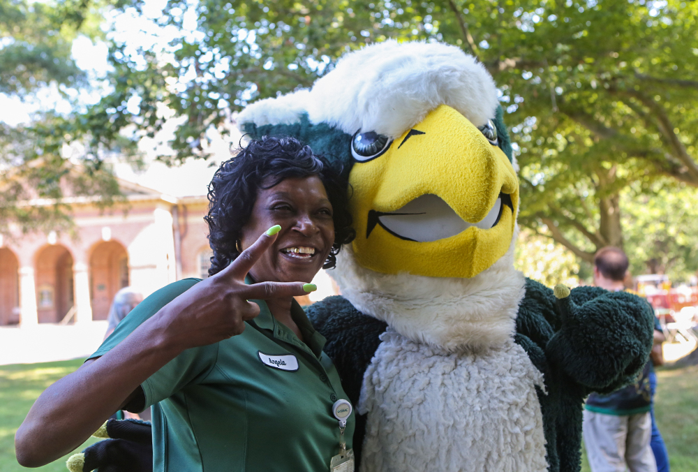 A William & Mary employee holds up a peace sign while standing next to Griffin, the W&M mascot.