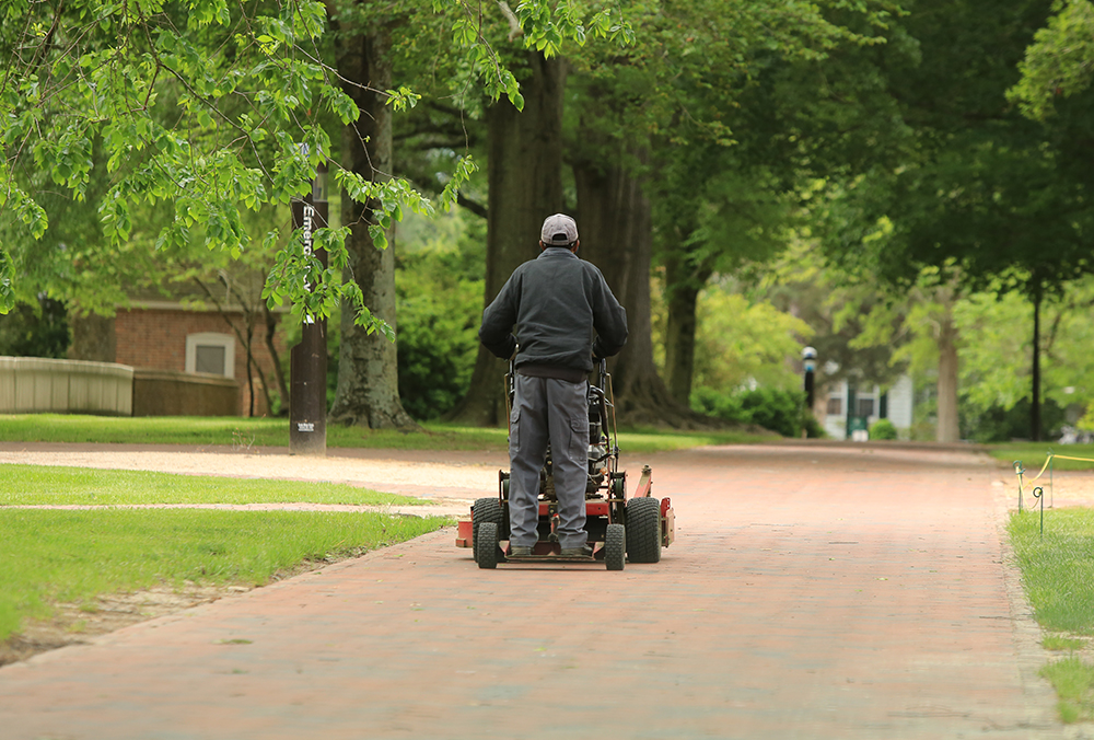 A William & Mary employee operating a lawn mower.