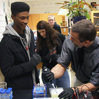 Emil Davis, biology teacher at Bruton High School, gets his students Kai Brown (front) and Brittany Cordero started on a gel electrophoresis experiment as William & Mary biologist Margaret Saha looks on. 