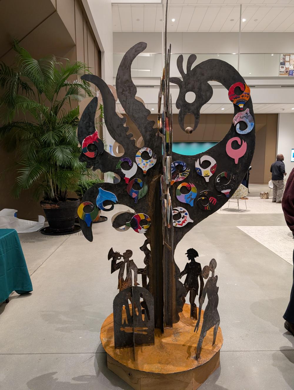 Large black Sankofa bird sculpture with smaller colorful pieces applied and celebratory figures at the base
