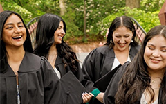 Four smiling, laughing students in Commencement regalia.