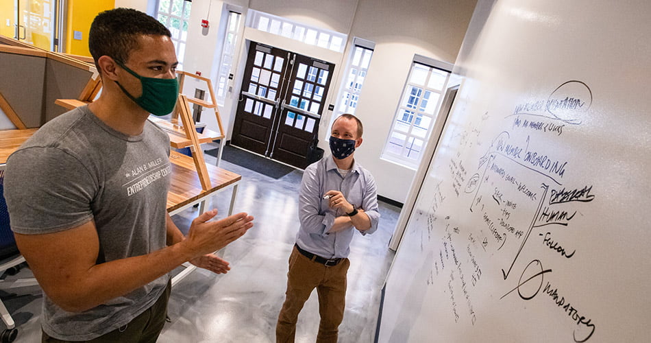 A masked student and Graham Henshaw discussing notes on a white board in W&M's Entrepreneurship Center in Tribe Square.