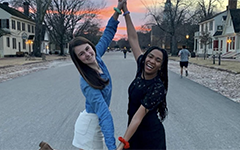 Two students smiling and joining hands with a Colonial Williamsburg sunset in the background