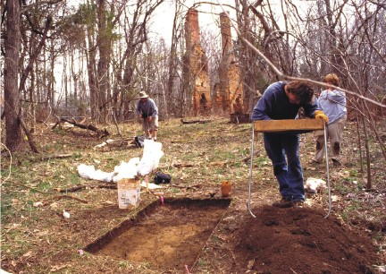 Archaeologists search for evidence of outbuildings near the main house. To make sure even small artifacts are found, soil is passed through wire mesh screen boxes like the one being used on the right.