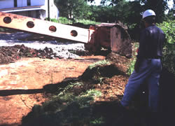 A Gradall operator carefully peels back the upper layers while an archaeologist watches closely for signs of features.