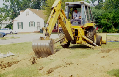 Guided by archaeologists, a skilled backhoe operator removes the mixed overburden in small increments.