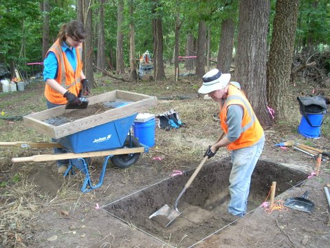 By gradually removing the soil within a test unit with flat shovels and trowels, archaeologists can document the natural stratigraphy and features, and keep separate drawings, notes, and bags of artifacts from each layer. While one archaeologist removes the soil and places it in a screen of quarter inch wire mesh, another carefully sifts the soil into a wheelbarrow and retrieves artifacts.
