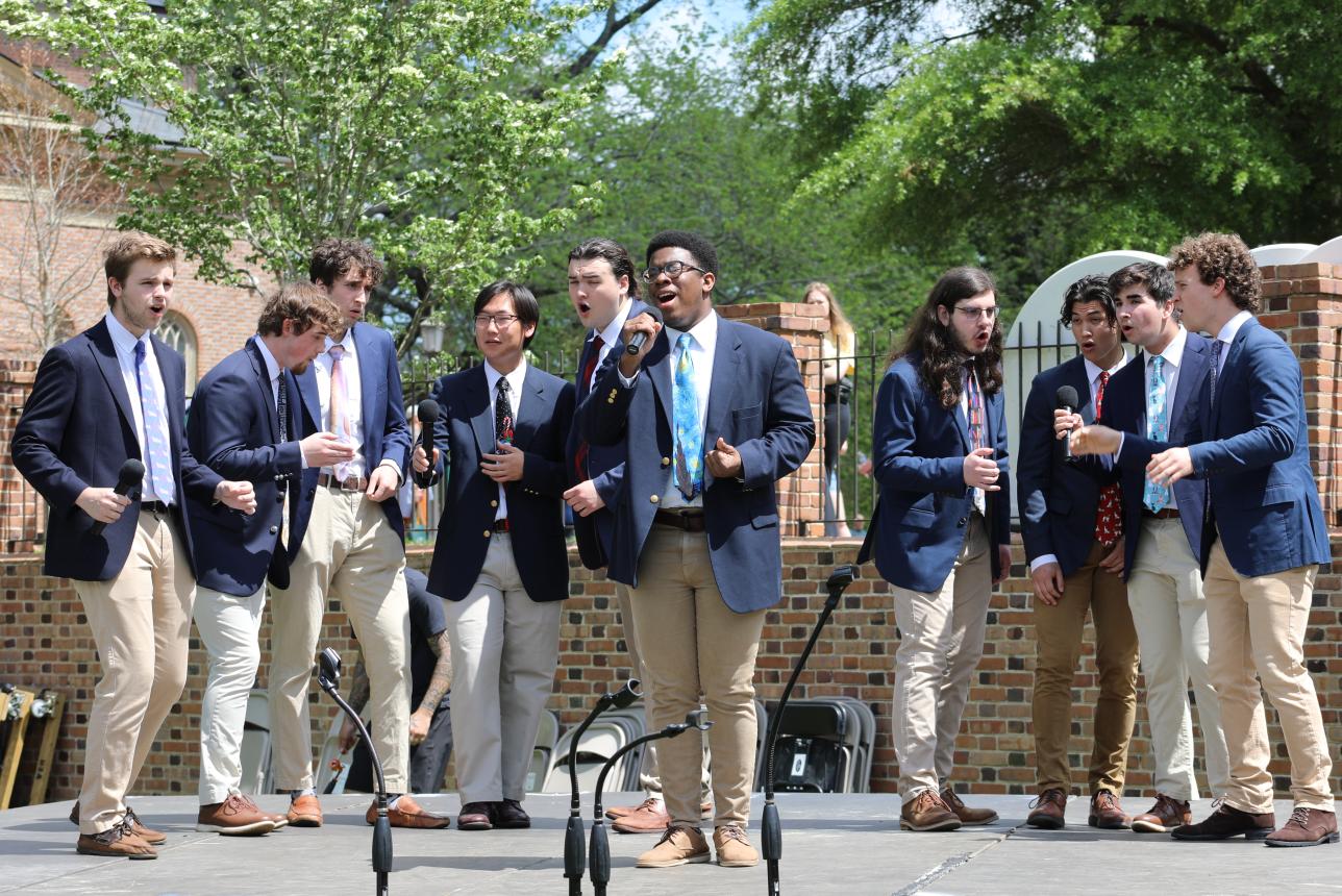 group of male students singing on stage outside