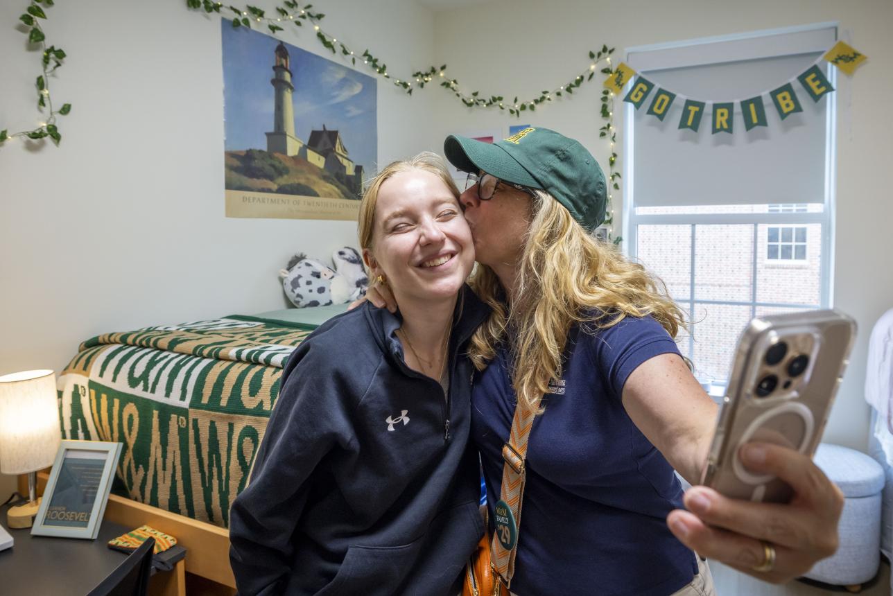 Mom kissing daughter on the cheek while taking a selfie in a newly-decorated dorm room